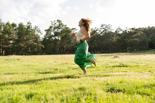 Saf bir özgürlük anını yakalayan bu genç kadın çayırda neşeyle koşuyor. Yeşil eteği gün batımında dalgalanan.. - Fotoğraf, Görsel