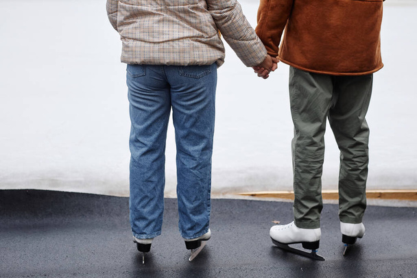 Achteraanzicht van een onherkenbaar koppel dat elkaars hand vasthoudt in een schaatsbaan, kopieerruimte - Foto, afbeelding