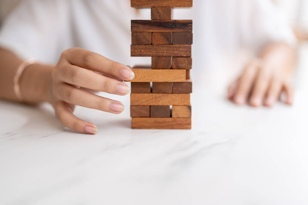 A close-up shot of a woman pays her attention on playing a wooden block game at a table, moving a wooden block. toy, game, leisure - Photo, Image