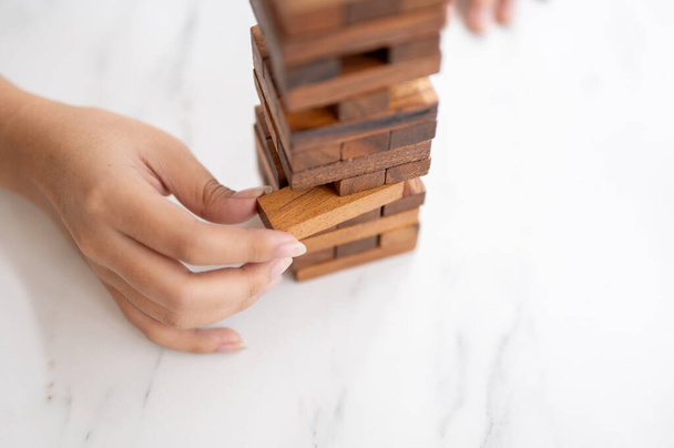 Un primer plano de una mujer presta atención a jugar un juego de bloques de madera en una mesa, moviendo un bloque de madera. juguetes, juegos, ocio - Foto, imagen