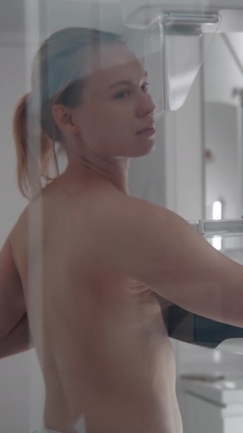 Caucasian adult woman stands topless in hospital radiology room. Female patient undergoing mammography screening checkup using digital mammograph. Breast cancer prevention. Modern clinic equipment. - Footage, Video