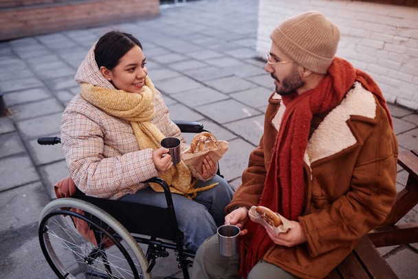 Porträt einer jungen Frau mit Behinderung, die im Winter mit ihrem Freund Streetfood-Snacks im Freien genießt - Foto, Bild