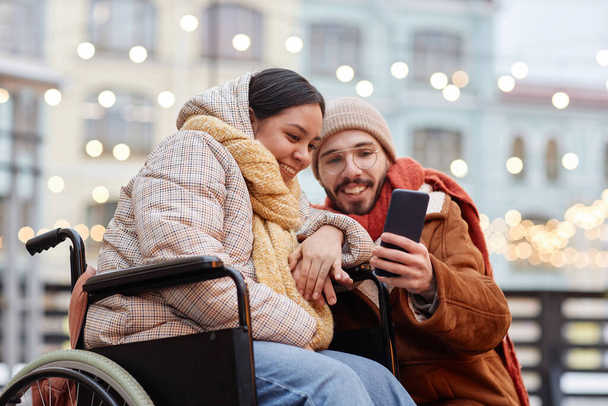 Portrait of young woman with disability taking selfie photo outdoors with boyfriend and using smartphone - Photo, Image