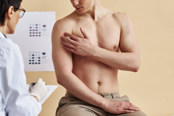 Lähikuva naisten ihotautilääkäri tutkii paidaton mies kuulemisen aikana klinikalla, kopioi tilaa - Valokuva, kuva