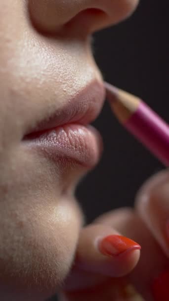 Lipmake-up. zijaanzicht. Close-up van een professionele make-up kunstenaar het aanbrengen van een gekleurd potlood om een mooie jonge vrouw te schetsen. meisje contouren sexy lippen. - Video