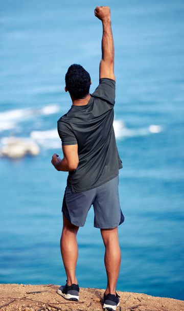Чоловік, пішохідні та гірські святкування на скелі з кулаком для перемоги на вправах або на відкритому повітрі, спини або тренування. Чоловік, пішохідні та медичні цілі в океані або досліджувати Австралію, подорожі або подорожі. - Фото, зображення