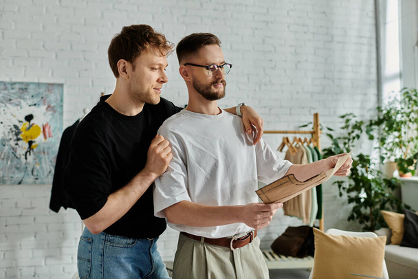 Deux hommes, un couple gay, se tiennent côte à côte dans un atelier de designer, créant passionnément des vêtements tendance ensemble. - Photo, image