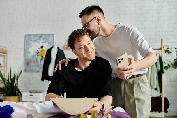 гей чоловік цілує голову хлопця в дизайнерській майстерні, співпрацюючи над створенням модного одягу разом. - Фото, зображення