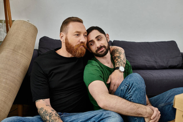 A couple of men sit comfortably on top of a couch in their new home - Photo, Image
