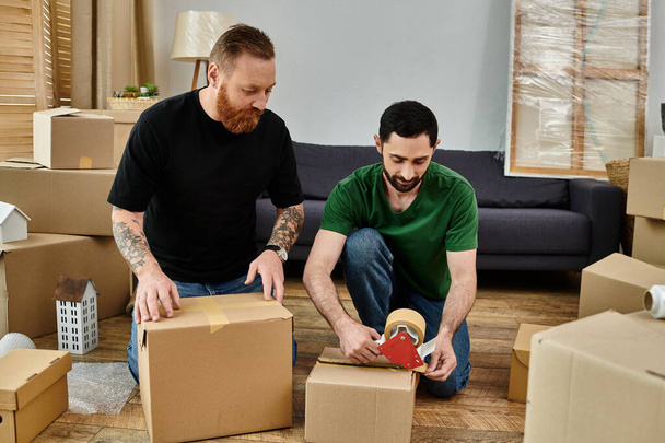 Two men sit on the floor surrounded by moving boxes, embracing the start of a new life in their new home. - Photo, Image