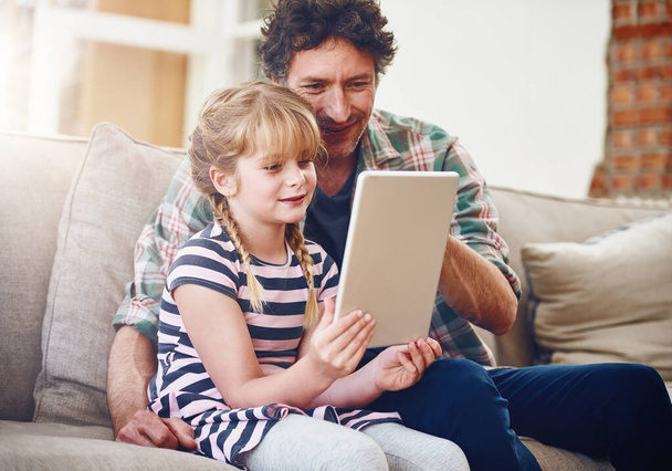 Otthon, apa és lánya táblagéppel a kanapén mosollyal a tanuláshoz, a gyermekfejlődéshez és a növekedéssel kapcsolatos tudáshoz. Szülő, gyerek és támogatás segítségével, oktatási és oktatási játék szórakoztató. - Fotó, kép
