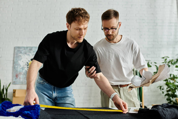 Δύο άνδρες στέκονται δίπλα-δίπλα σε ένα εργαστήριο σχεδιαστών, που συνεργάζονται για τη δημιουργία της μόδας ενδυμασία. - Φωτογραφία, εικόνα