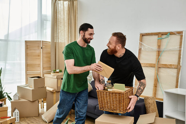 Two men, a gay couple in love, stand side by side in a room surrounded by boxes, starting a new life in their new home. - Фото, изображение