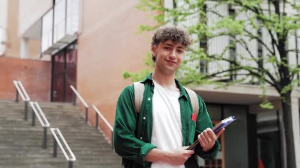 Πορτρέτο του χαμογελαστού φοιτητή που στέκεται στην πανεπιστημιούπολη. Ευτυχής κοιτάζοντας την κάμερα έτοιμη για διάλεξη - Πλάνα, βίντεο