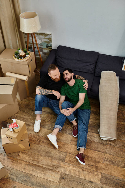 A man and a woman, a gay couple in love, sit on the floor amidst moving boxes in their new living room. - Foto, Imagem