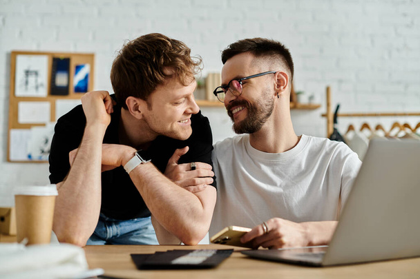 Двое мужчин, гей-пара, сидят вместе за столом, сосредоточившись на экране ноутбука в мастерской дизайнера. - Фото, изображение