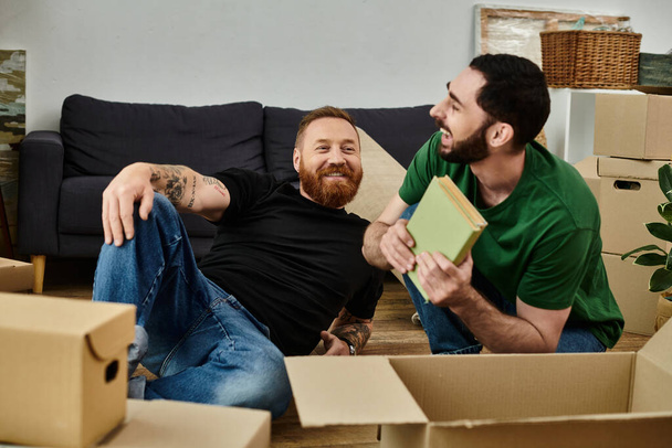 Paar mannen, een homo koppel, ontspannen op de dozen in hun nieuwe huis, omgeven door verhuisdozen in een teken van een nieuw hoofdstuk. - Foto, afbeelding