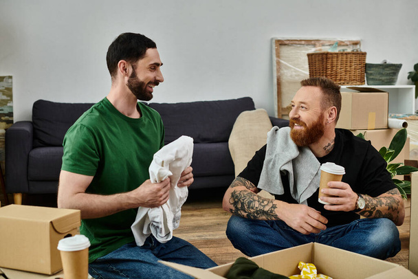 A gay couple in love takes a break, sitting atop a couch surrounded by moving boxes in their new home. - Foto, immagini