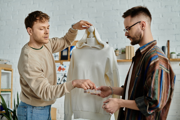 Két férfi áll egy próbababa mellett egy tervező műteremben, bemutatva trendi öltözéküket.. - Fotó, kép
