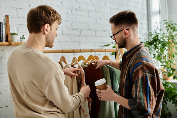 Deux hommes, un couple gay, se tiennent côte à côte dans un atelier de designers, collaborant sur des vêtements tendance. - Photo, image