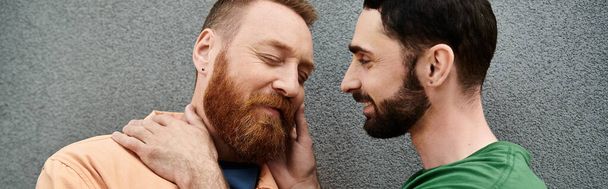 Een portret van een homoseksueel stel in casual kleding, naast elkaar staan tegen een grijze muur. - Foto, afbeelding