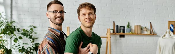 Δύο άνδρες, ένα γκέι ζευγάρι, στέκονται δίπλα-δίπλα σε ένα εργαστήριο σχεδιαστών, συνεργαζόμενοι με τις μοντέρνες δημιουργίες ενδυμασίας τους.. - Φωτογραφία, εικόνα