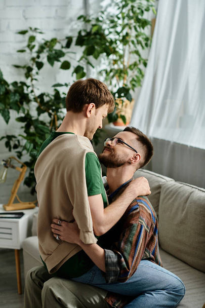 Kaksi miestä, jotka ovat osa homoparia, istuvat tyylikkään sohvan päällä suunnittelijatyöpajassa, halaavat rakkaudella. - Valokuva, kuva
