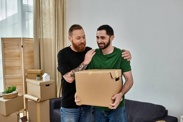 Homopariskunta seisoo yhdessä olohuoneessa ympäröivät muuttolaatikot, alkaen tuoreena uudessa kodissa. - Valokuva, kuva