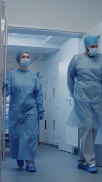 Enfermera y paramédico abren puertas de pasillo de instalaciones médicas. Cirujanos multiétnicos empujan camilla con paciente anciano mentiroso al quirófano. El personal médico trabaja en urgencias. Vertical - Imágenes, Vídeo