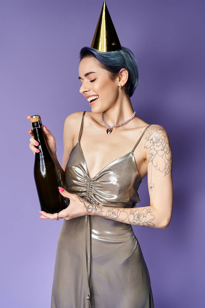 Young woman with short blue hair wearing a silver party dress, holding a bottle while sporting a party hat. - Fotografie, Obrázek