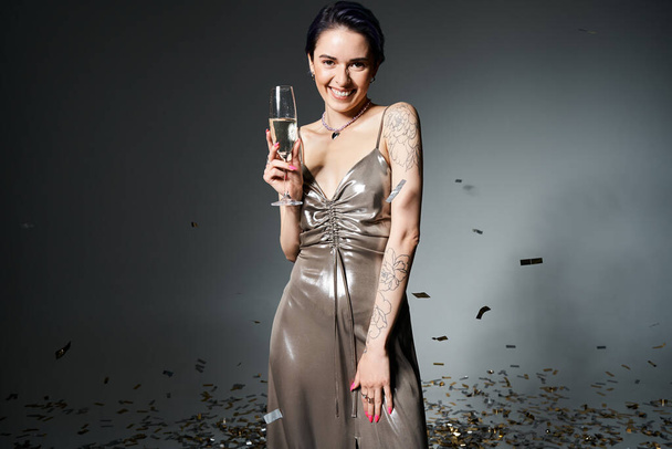 Young woman with short blue hair striking a pose in a silver dress while holding a glass of champagne. - Valokuva, kuva