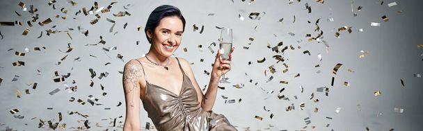 A young woman with short blue hair elegantly holds a glass of champagne in a silver party dress. - Foto, immagini