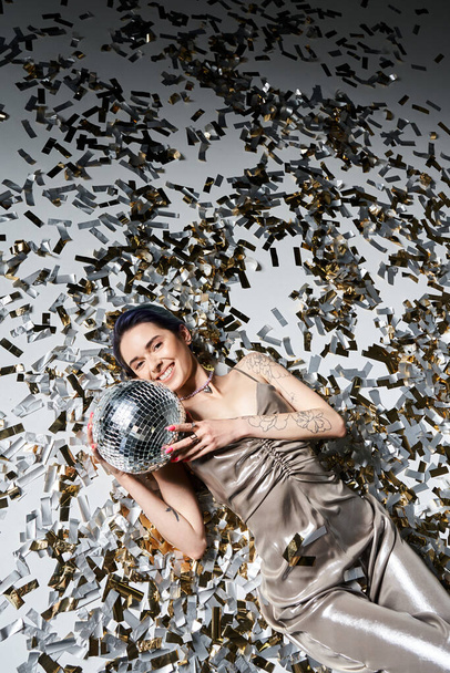 A pretty young woman with short blue hair lays on the ground, gracefully holding a shimmering disco ball. - Foto, immagini