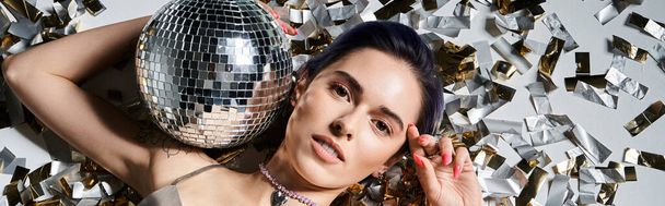 A pretty young woman with short blue hair holds a disco ball in front of her face, surrounded by a silver party dress. - Photo, Image