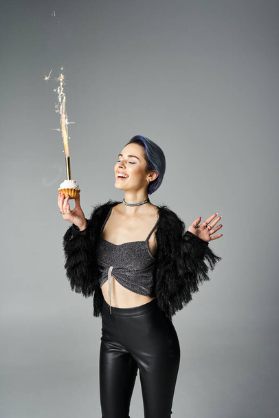 A young woman with short dyed hair wearing black pants and a crop top, playfully holds a sparkler in a studio setting. - Фото, зображення