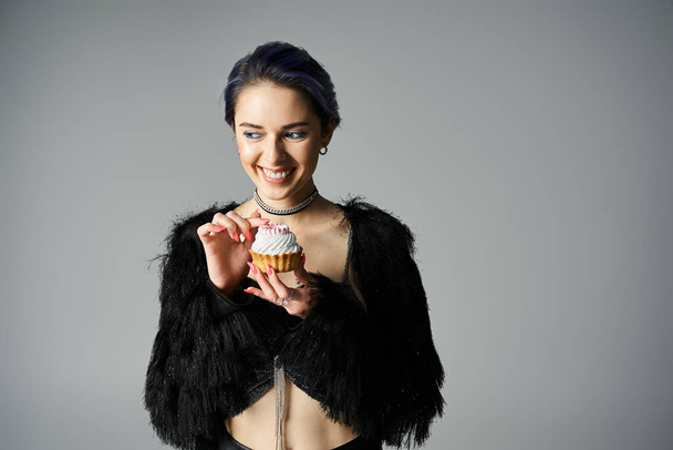 A pretty young woman with short dyed hair holds a colorful cupcake in her hands, admiring its intricate design. - Фото, изображение