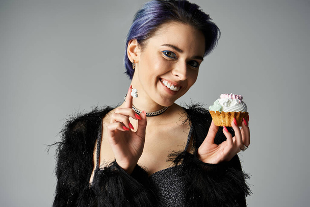 A young woman with blue hair holding a delicious cupcake in a studio setting, exuding a festive birthday vibe. - Foto, imagen