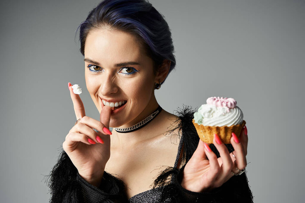 Stylish young woman holds a cupcake, exuding an air of sophistication and rebellion. - Foto, imagen