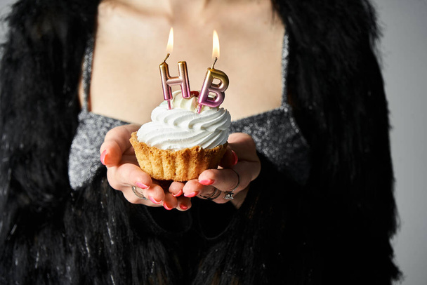 A stylish young woman with short dyed hair holding a cupcake with burning candles in a studio setting. - Photo, Image