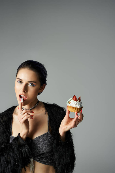 A stylish young woman with dyed hair poses with a cupcake, taking a bite from it. - Fotografie, Obrázek