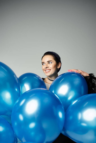 A stylish birthday girl with short dyed hair delicately holds a bunch of vibrant blue balloons. - Φωτογραφία, εικόνα