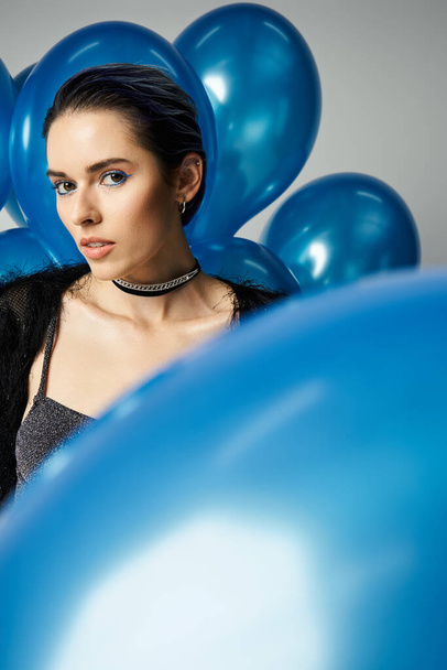A young woman with short dyed hair poses elegantly in front of a bunch of blue balloons. - 写真・画像