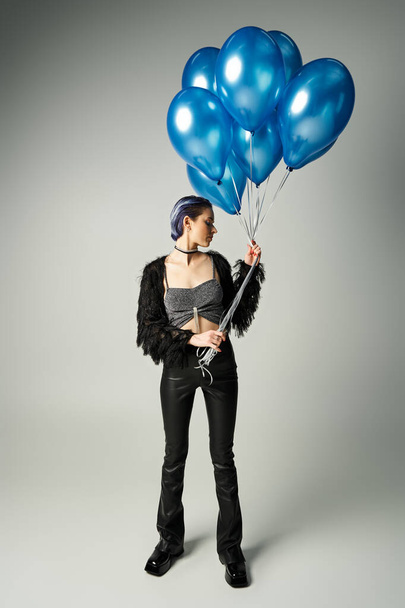 A young woman with short dyed hair holding a bunch of blue balloons, radiating joy and celebration in a studio setting. - Photo, image