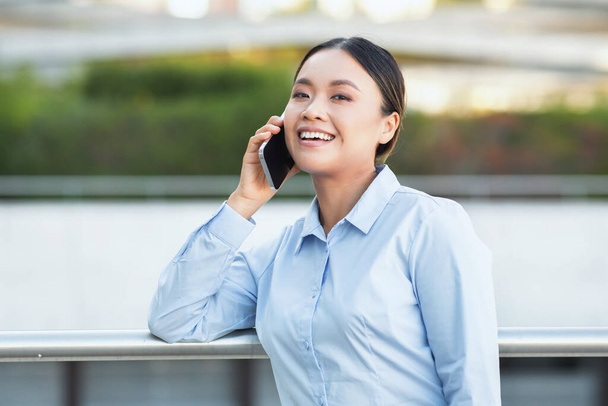 Una donna d'affari asiatica è impegnata in una conversazione telefonica, trasmettendo professionalità e concentrazione. Lei è visto multitasking pur mantenendo un comportamento commerciale - Foto, immagini