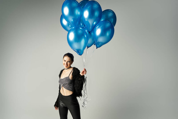A stylish young woman, the birthday girl, smiling while holding a bunch of vibrant blue balloons. - Foto, Imagen