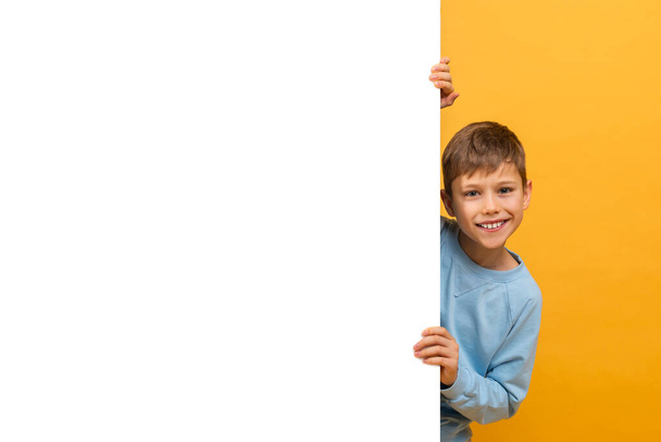 Op deze foto is een jongetje afgebeeld met een wit bord. Hij lijkt buiten te staan, met een serieuze uitdrukking op zijn gezicht als hij het bord stevig vastgrijpt. Het bord is leeg. - Foto, afbeelding
