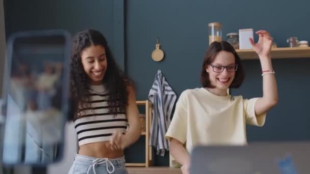 Μέτριο πλάνο του χαρούμενου Καυκάσιου έφηβος κορίτσι με εγκεφαλική παράλυση γυρίσματα κλιπ χορού για τα μέσα κοινωνικής δικτύωσης με Biracial θηλυκό φίλο στο smartphone, ενώ περνούν ελεύθερο χρόνο στο σπίτι μαζί - Πλάνα, βίντεο