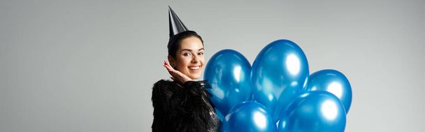 A stylish young woman with short dyed hair poses with a bunch of blue balloons in a studio setting. - 写真・画像