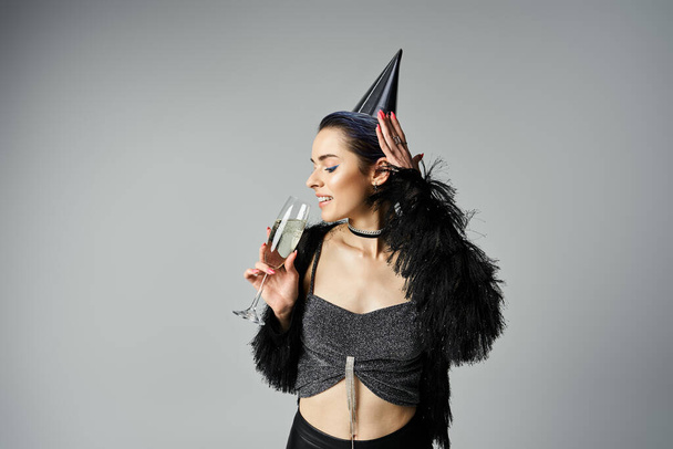 A young woman with short dyed hair dons a party hat while elegantly holding a glass of champagne - Фото, изображение