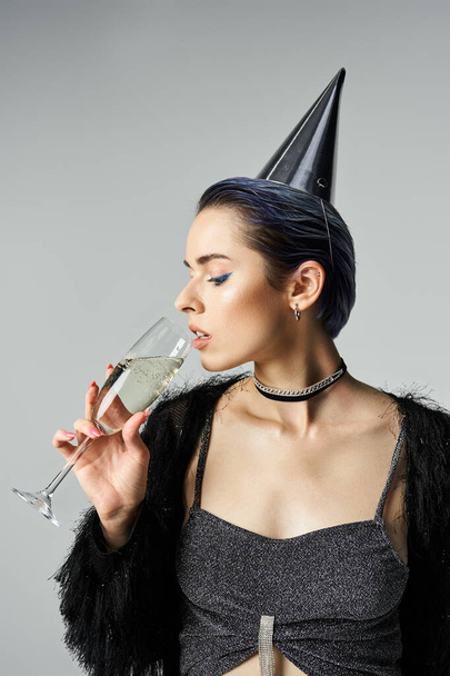 A stylish young woman with short dyed hair, wearing a party hat, holding a champagne glass. - Foto, Bild
